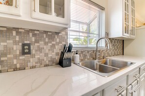 Una cocina con salpicadero de azulejos, un lavamanos de acero inoxidable y armarios blancos.