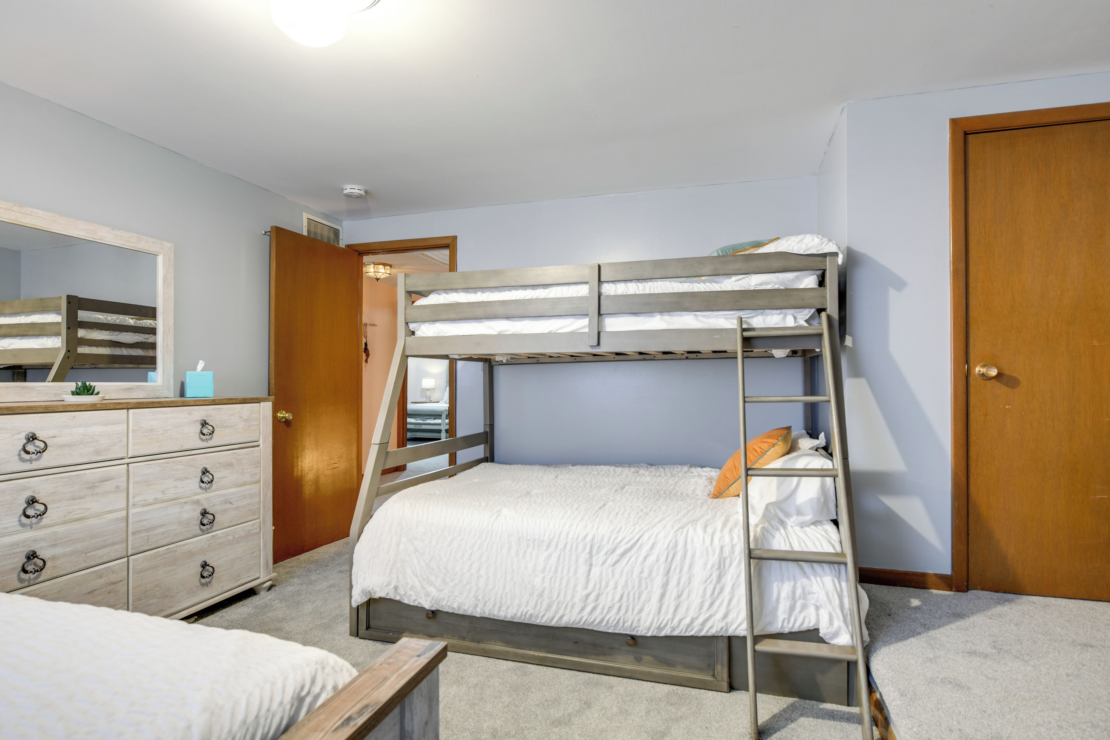 Een slaapkamer met een stapelbed, een houten dressoir, een spiegel en een deur.