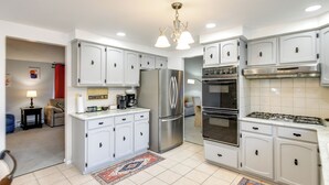 A modern kitchen with white cabinets, stainless steel appliances, and a chandelier. - Deck & Seasonal Pool: Spacious Home Near Buffalo! (Buffalo)