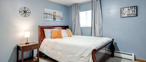A bedroom with a bed, bedside table, lamp, and artwork on the walls.