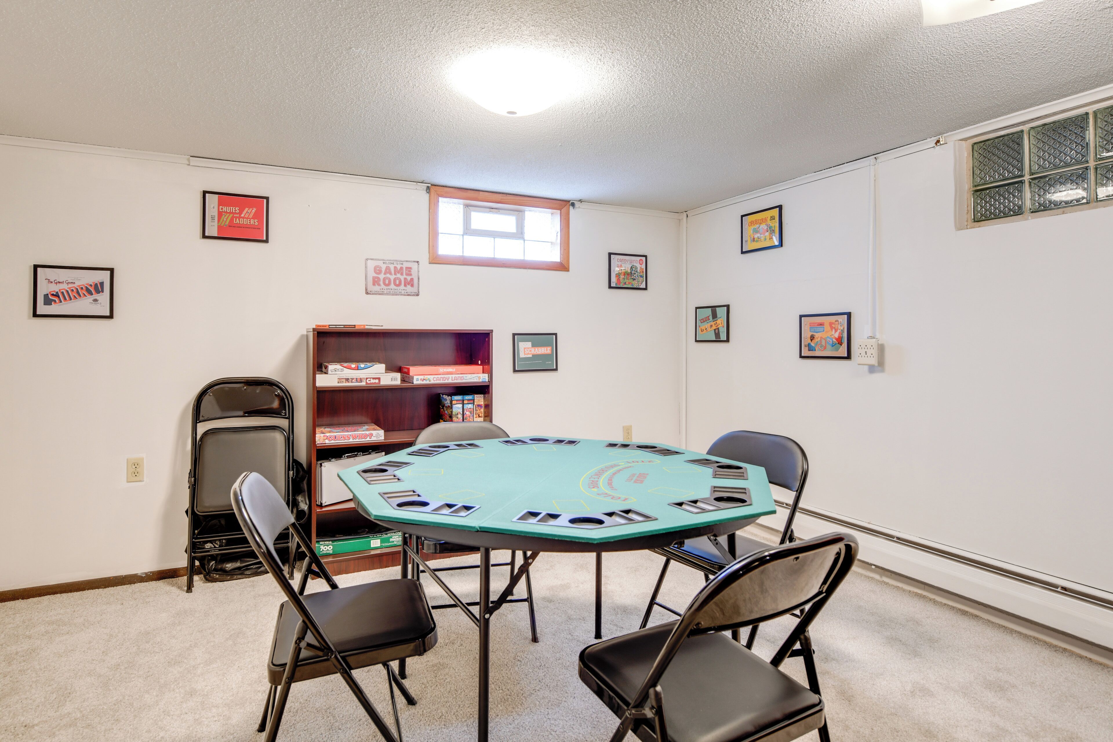 A room with a round table, four chairs, a bookshelf, and framed pictures on the walls.
