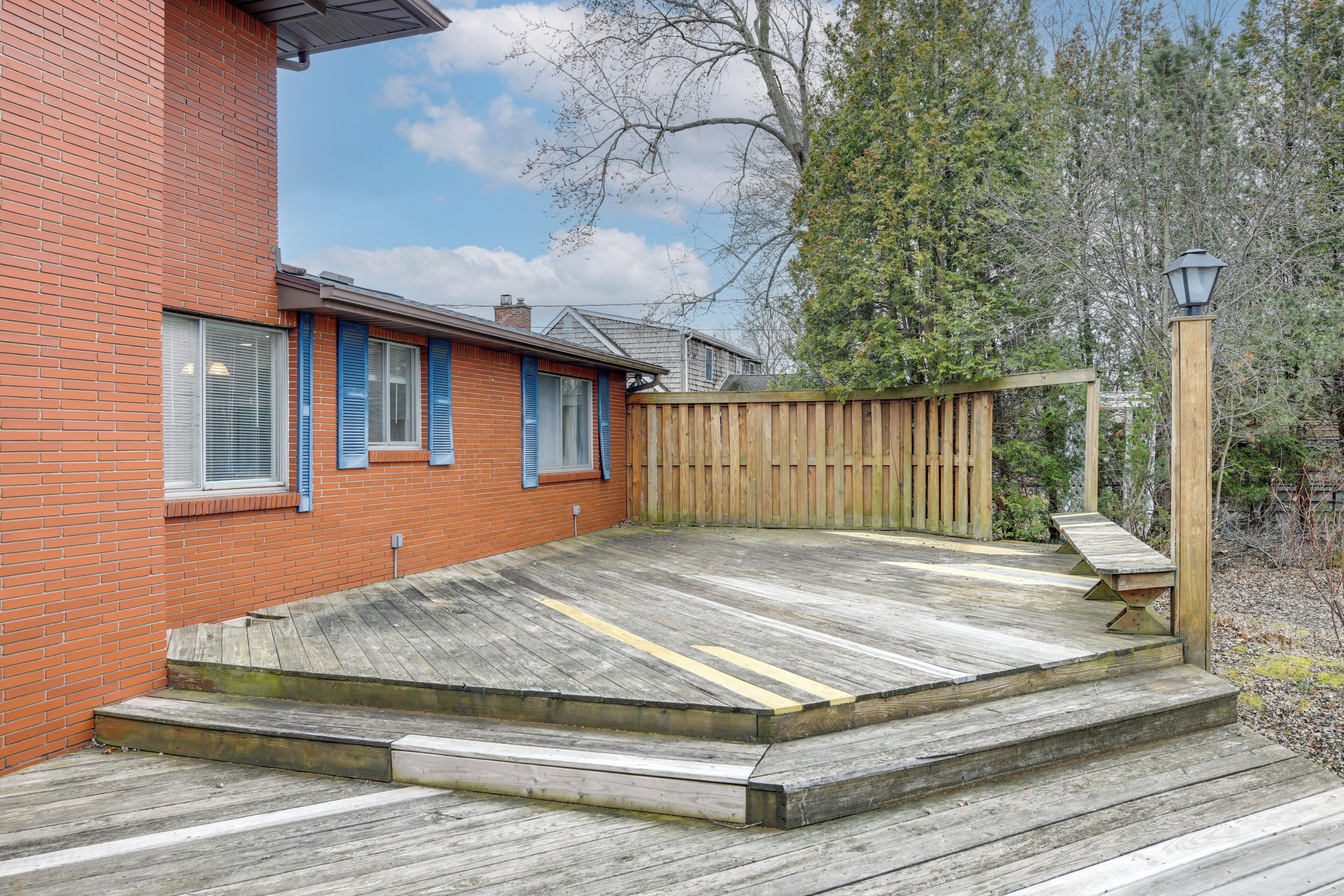 A wooden deck with steps leading to a wooden fence, adjacent to a brick building with blue shutters.