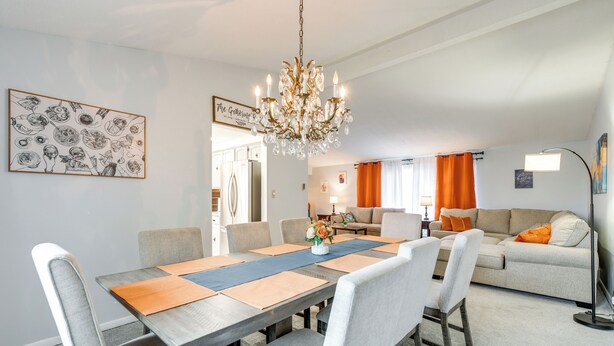 A dining area with a wooden table, beige chairs, and a chandelier. - Deck & Seasonal Pool: Spacious Home Near Buffalo! (Buffalo)