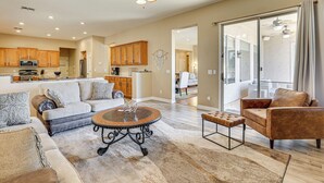 A spacious living area with a sofa, coffee table, and a brown leather chair. A kitchen with wooden cabinets and a dining area are visible in the background. - Peoria Desert Oasis < 10 Mi to Spring Training! (Peoria)