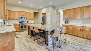 A spacious kitchen with wooden cabinets, a granite island with bar stools, stainless steel appliances, and a tiled floor. - Peoria Desert Oasis < 10 Mi to Spring Training! (Peoria)