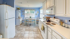 A kitchen with a refrigerator, stove, microwave, and dining table with chairs. - Swim, Fish & Explore: Marsh-front Gem in Delaware! (Ocean View)