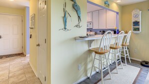 A kitchen with white cabinets, a bar area with white bar stools, and decorative wall art. - Swim, Fish & Explore: Marsh-front Gem in Delaware! (Ocean View)