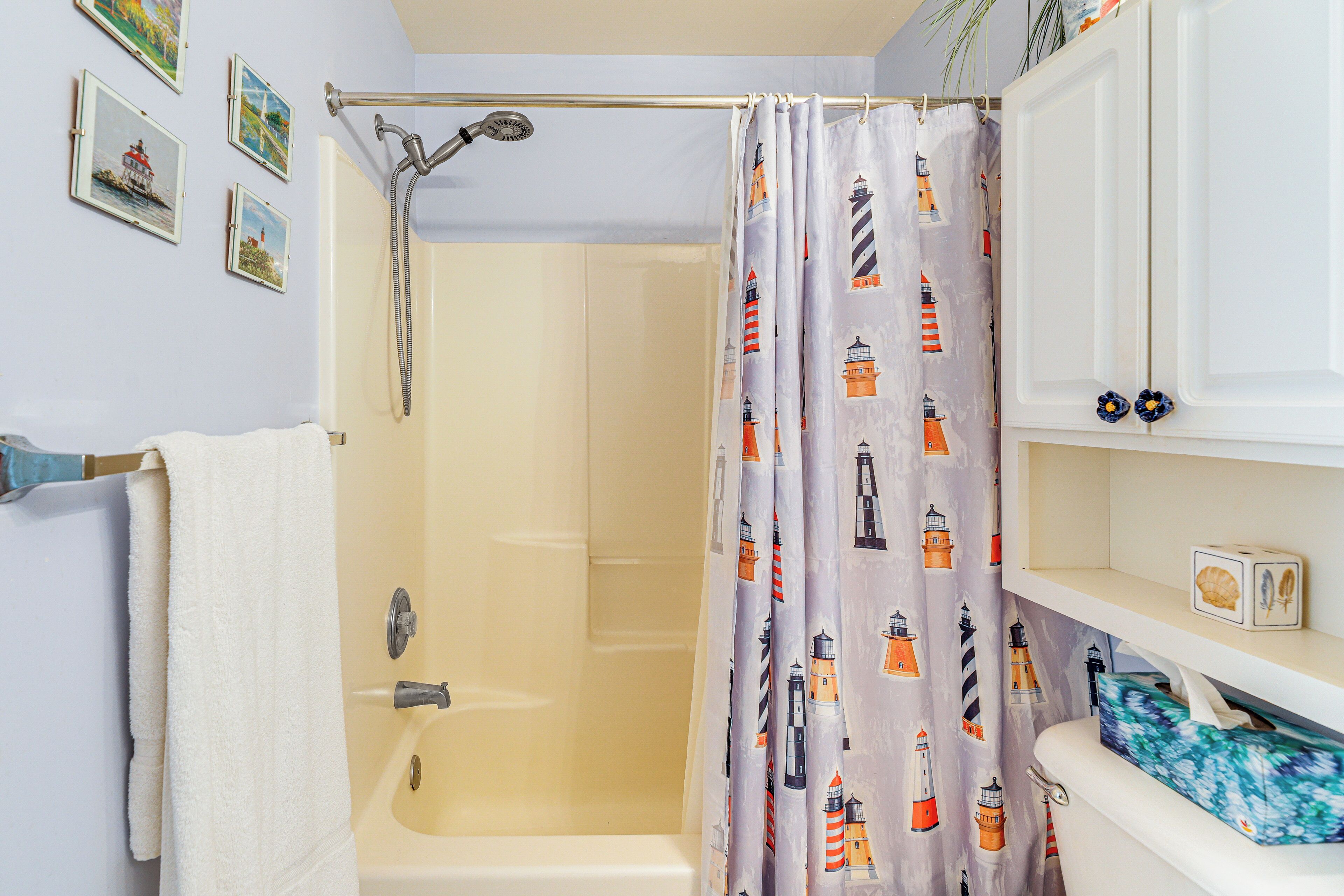 Baño con cortina de ducha estampada con faros, una bañera blanca y un perchero con una toalla blanca.