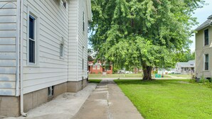 A residential street with a sidewalk, a large tree, and houses with white siding. - < 1 Mi to Main St: Quiet Apartment in Galesburg! (Galesburg)