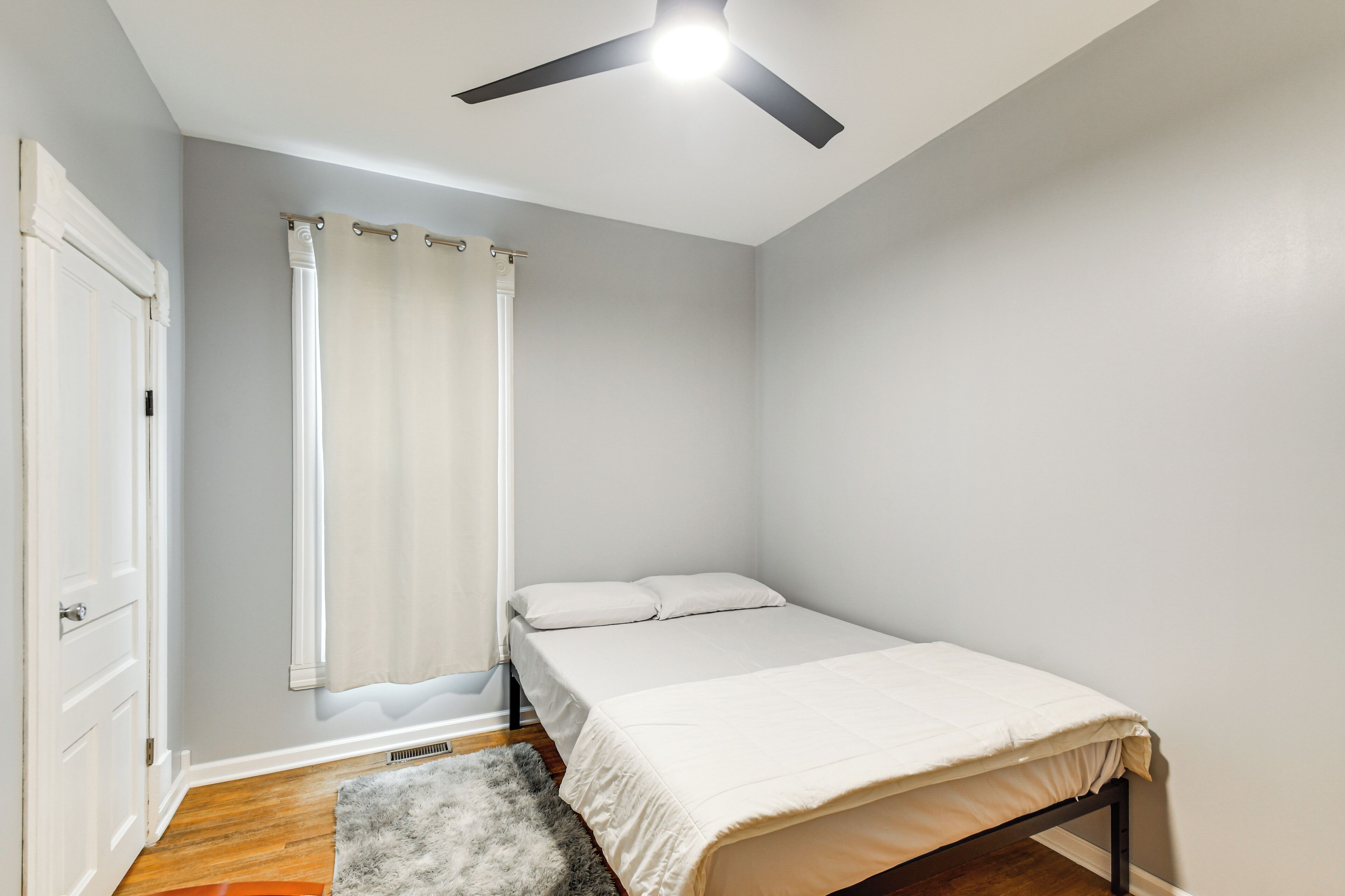 Un dormitorio con cama, ventilador de techo, ventana con cortinas y puerta.