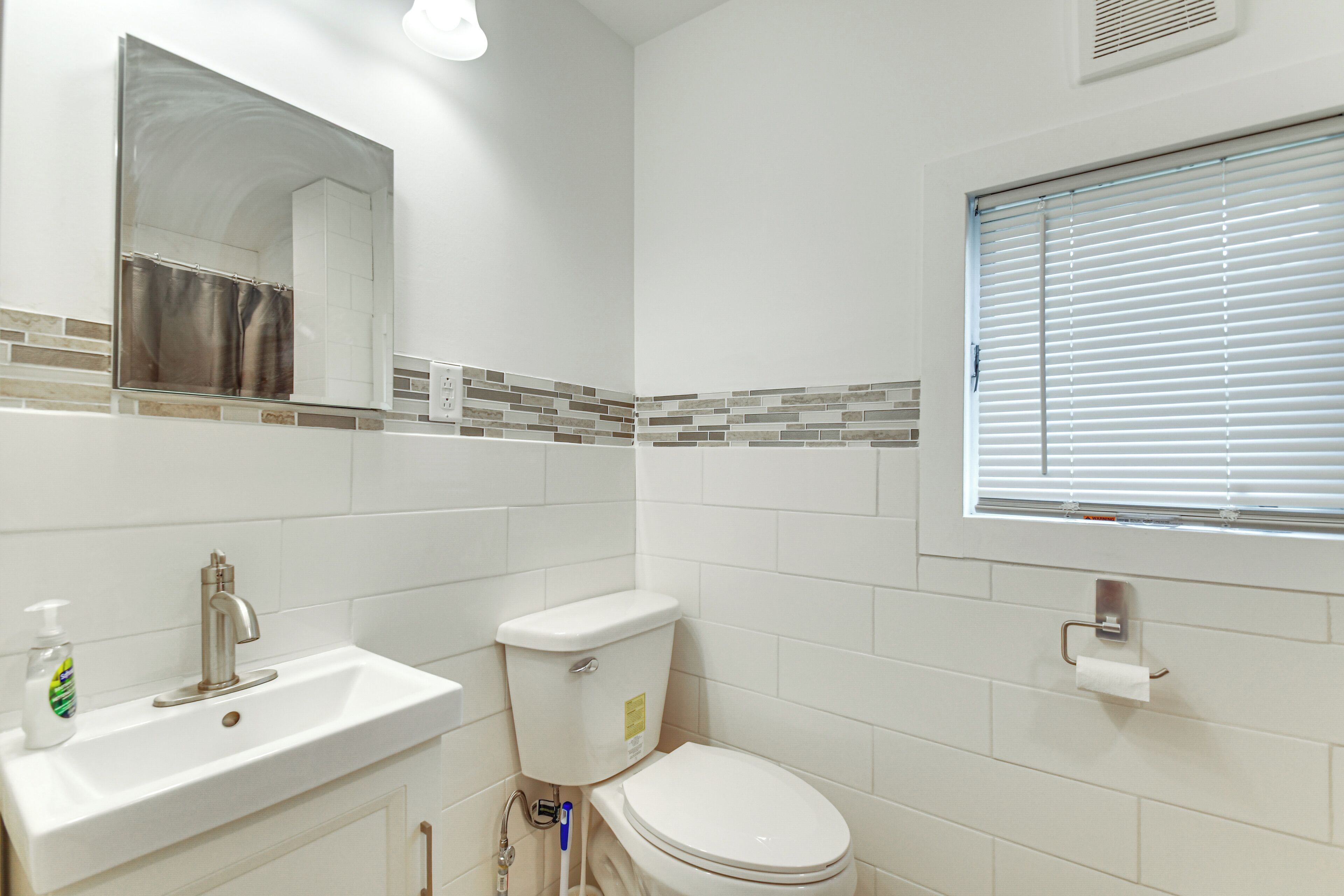 A bathroom with a white sink, toilet, and a mirror above the sink.