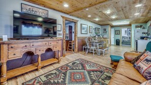 A spacious living room with a wooden ceiling, a television, a dining area, and a kitchen visible in the background. - Quiet Eagar Retreat Near Lakes, Hiking & Hunting! (Eagar)