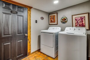 Un lavadero con dos lavadoras de carga frontal, una puerta de madera con letrero de salida de emergencia y obras de arte colgadas en la pared.