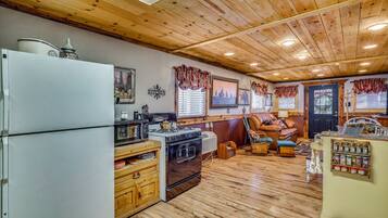 A kitchen with wooden cabinets, a refrigerator, a stove, and a dining area with a chair and table.