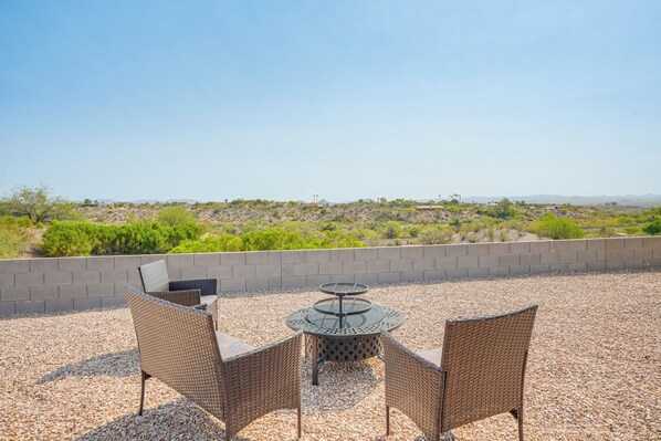 An outdoor patio with wicker furniture and a round table, overlooking a desert landscape.