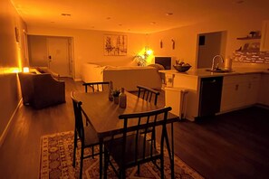 A modern living room with a dining table and chairs, a sofa, and a kitchen area with a sink and countertop.