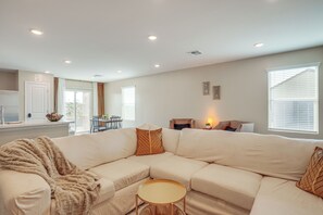 A modern living room with a beige sectional sofa, a small round table, and a kitchen area in the background.