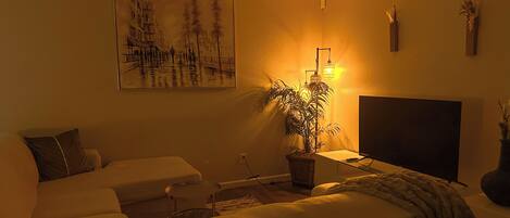 A cozy living room with a sofa, a TV, a plant, and a painting on the wall.
