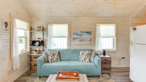 A cozy cabin interior with a teal sofa, wooden shelves, a small table, and a refrigerator. - 2 Mi to Carrabelle Beach: Home w/ Yard & Porch (Carrabelle)