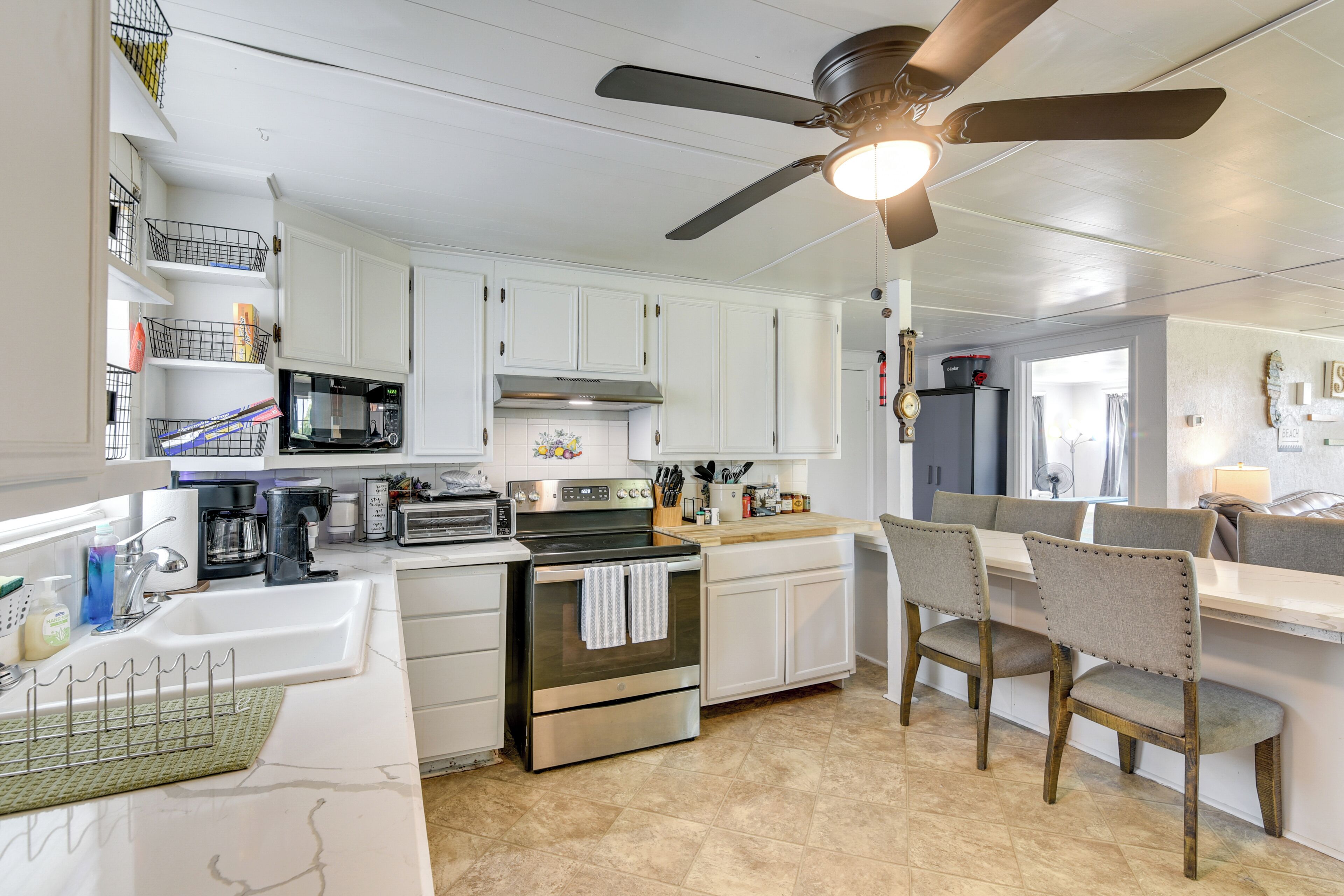 A kitchen with white cabinets, a microwave, stove, and a ceiling fan.