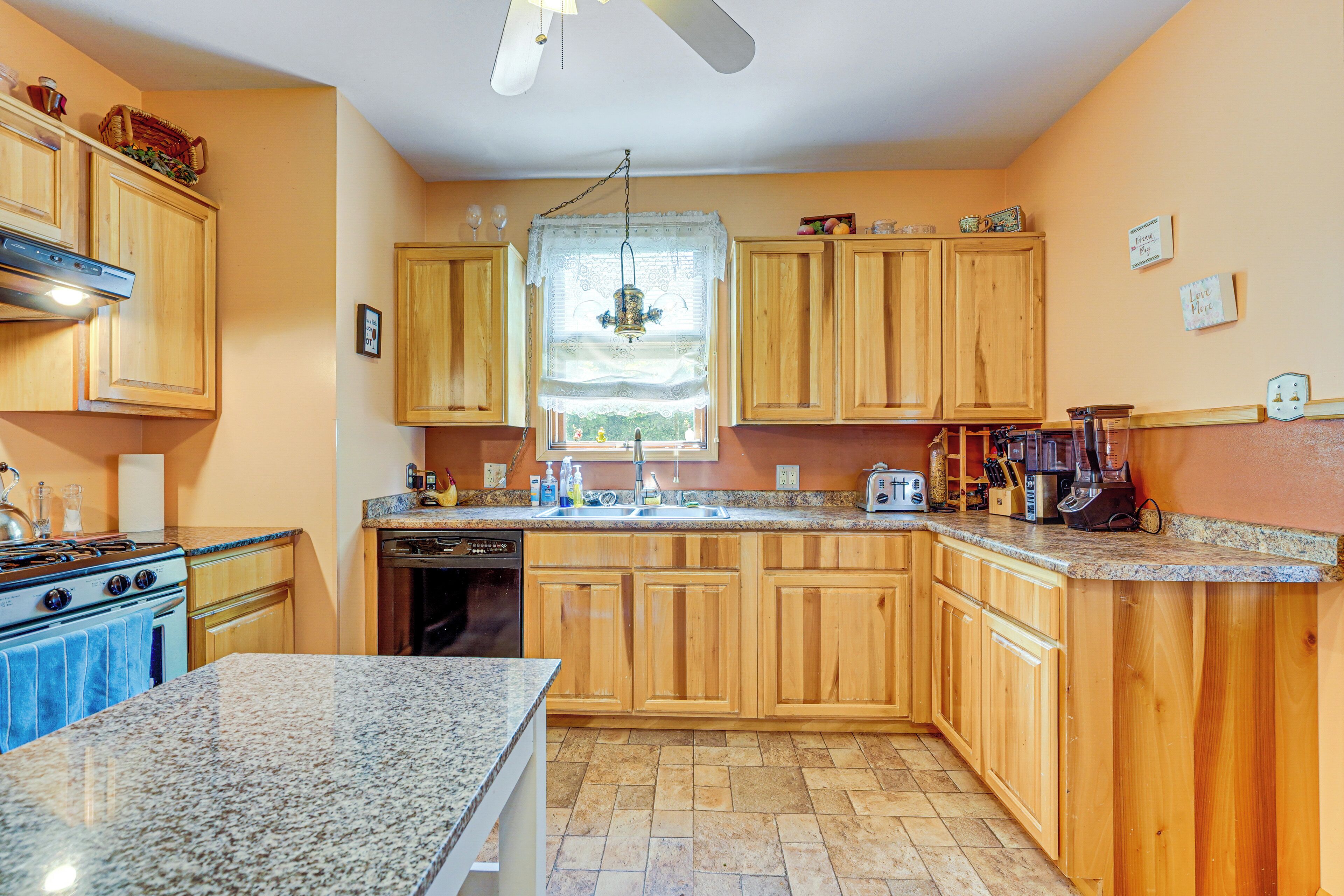 A kitchen with wooden cabinets, granite countertops, a built-in oven, and a window with a lace curtain.
