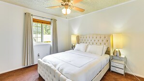 A bedroom with a tufted headboard, a large bed, two bedside tables with lamps, a ceiling fan, and a window with curtains. - 2 Mi to Historic Dtwn Nacogdoches: Cozy Apartment! (Nacogdoches)