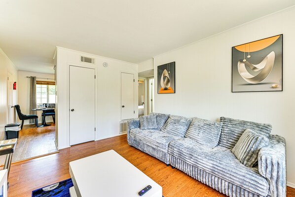A modern living room with a large sectional sofa, a white coffee table, and a framed abstract painting on the wall. - 2 Mi to Historic Dtwn Nacogdoches: Cozy Apartment! (Nacogdoches)
