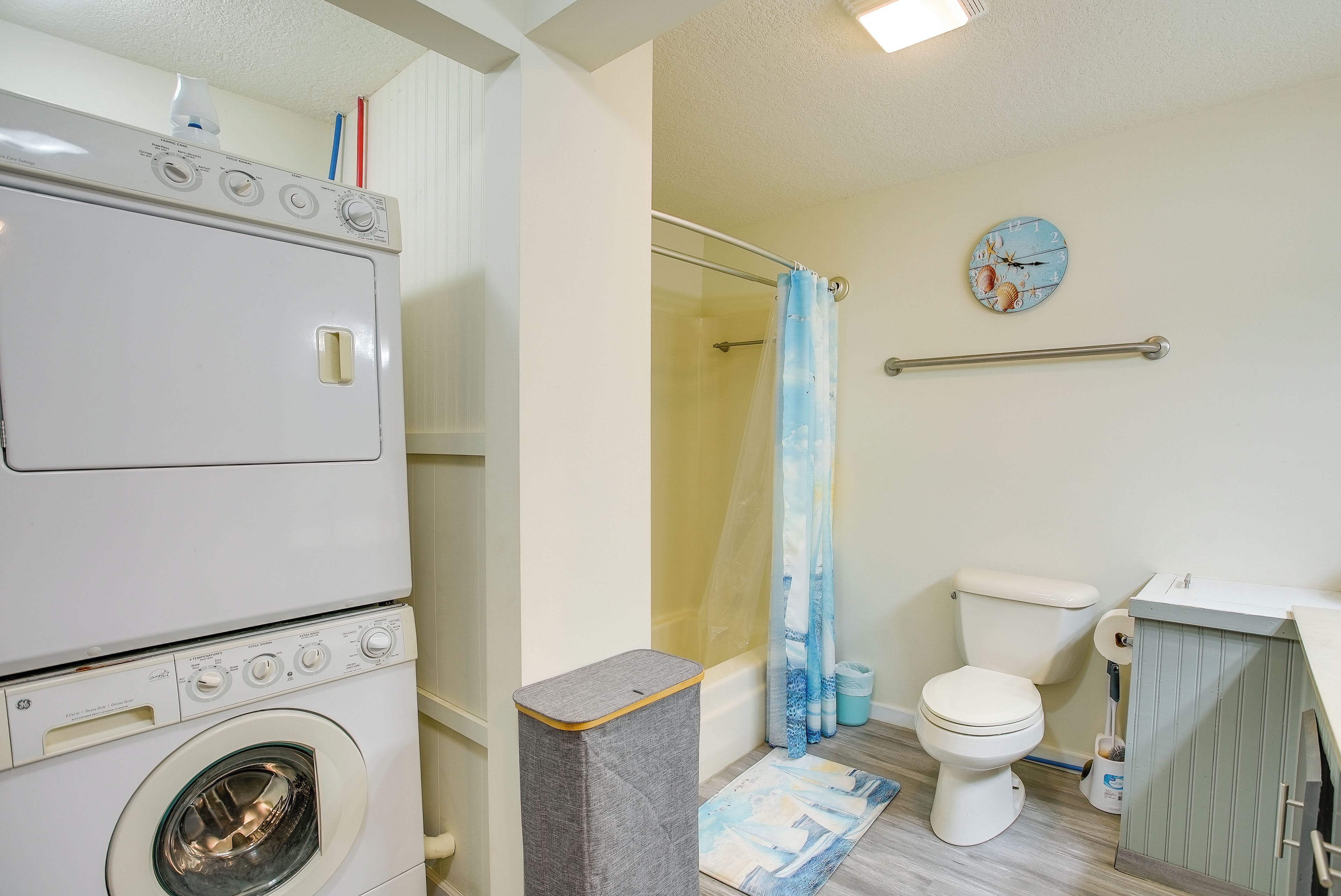Ein kleines Badezimmer mit Waschmaschine, Toilette, Dusche und einer Wanduhr.