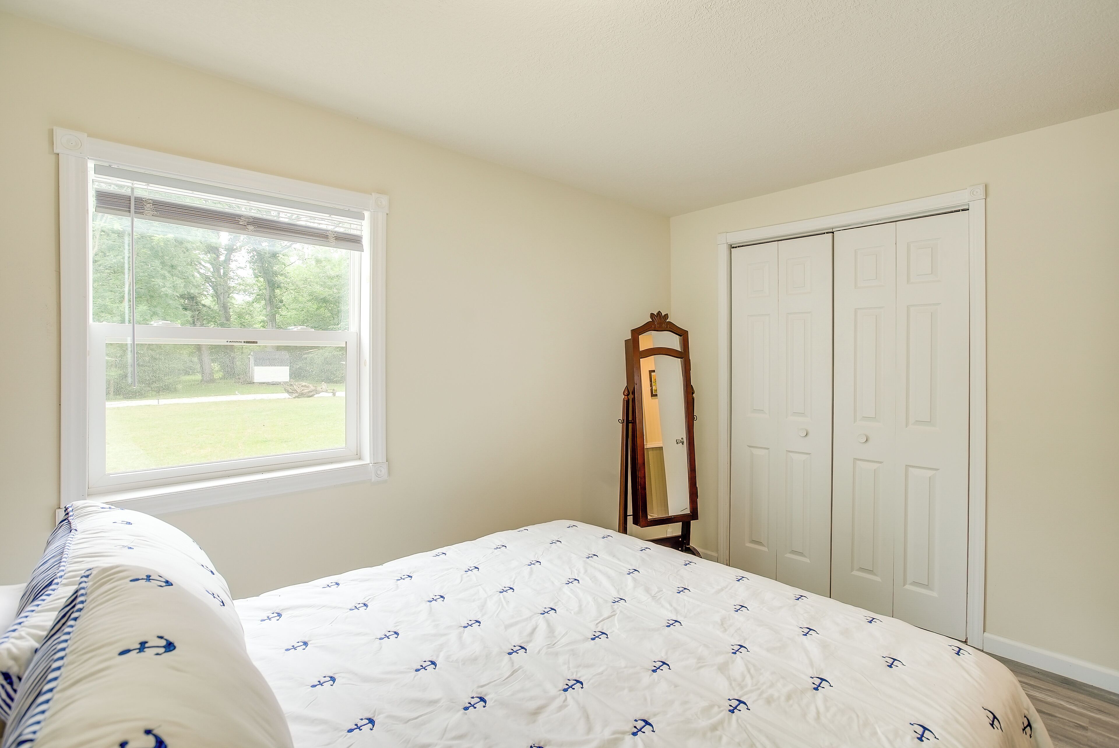 Ein Schlafzimmer mit Bett, Fenster, Spiegel und Kleiderschrank.