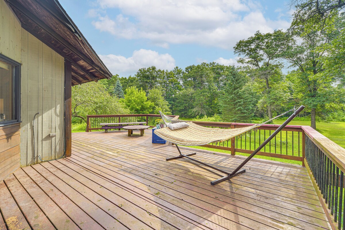 A wooden deck with a hammock, picnic table, and a view of a green landscape.
