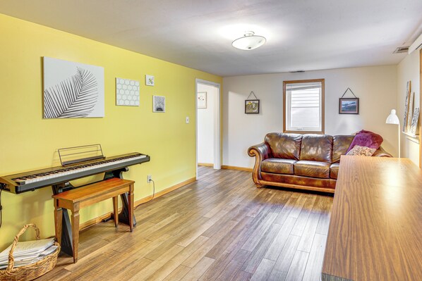 A living room with a piano, a leather sofa, and a wooden coffee table. - Walk to Spring Lake w/ Waterpark: Family Retreat! (Mankato)