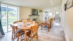 A spacious living room with a fireplace, a dining area with wooden furniture, and a kitchen in the background.