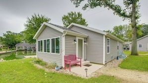 A single-story house with a covered porch, a small pond, and a red bench.