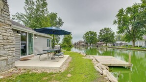 A lakeside patio with a table and umbrella, a dock, and a stone wall.