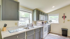 A kitchen with grey cabinets, a white countertop, and a window.