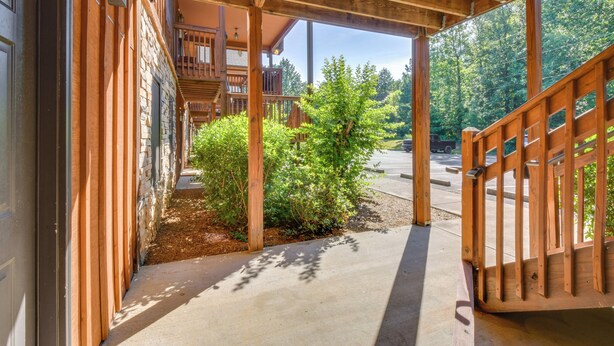 A covered wooden walkway leading to a building with a stone facade and a wooden deck. - Scenic Outdoor Space: Lake Keowee Retreat! (Six Mile)