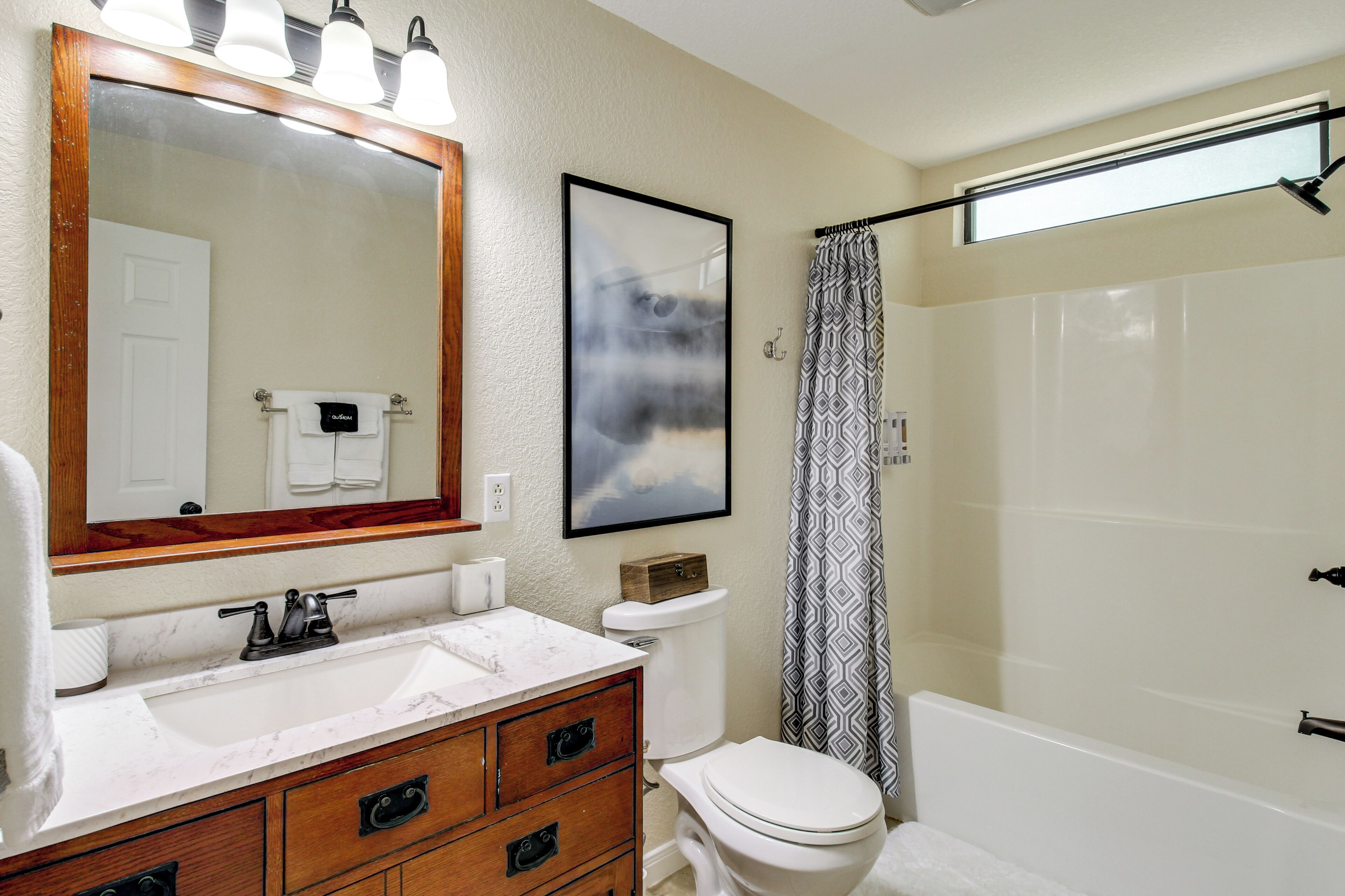 A bathroom with a large mirror, a sink with a marble countertop, a toilet, and a shower with a patterned curtain.