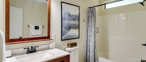 A bathroom with a large mirror, a sink with a marble countertop, a toilet, and a shower with a patterned curtain.