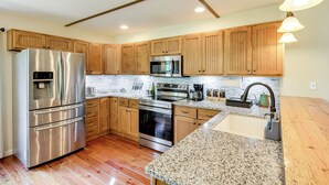 A modern kitchen with wooden cabinets, stainless steel appliances, granite countertops, and a built-in oven. - Dock & Hot Tub: Tennessee River Cabin Getaway (Whitwell)