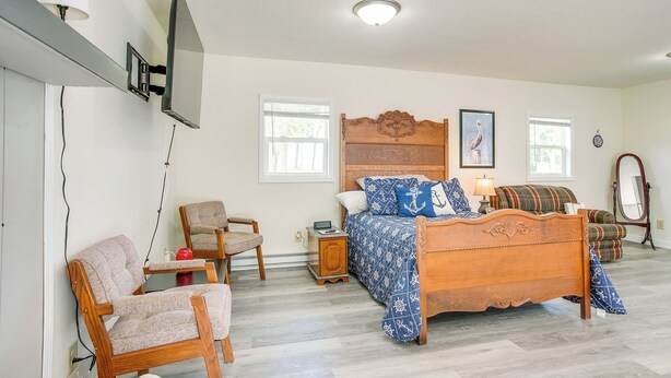 A bedroom with a wooden bed, a chair, a nightstand, a television, and a window. - Boat Dock: Couple's Grand Lake Getaway! (St. Marys)