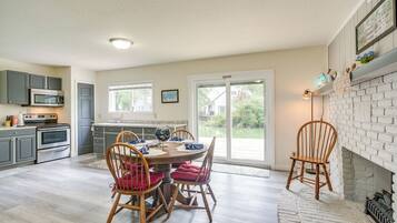 A kitchen with modern appliances, a dining area with wooden chairs, and a view of a house through a glass door.