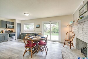 Una cocina con electrodomésticos modernos, un comedor con sillas de madera y vistas a una casa a través de un vidrio.