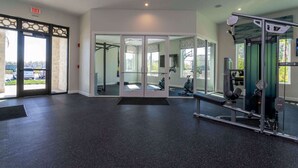 Ein Fitnessraum mit Spiegelwand, Trainingsgeräten und einer Tür, die nach draußen führt.
