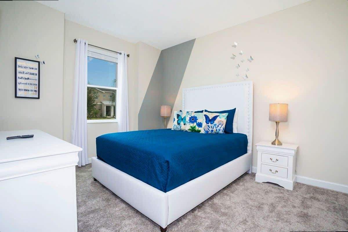 Une chambre à coucher avec un lit, une table de chevet, un bureau et une fenêtre avec des rideaux.