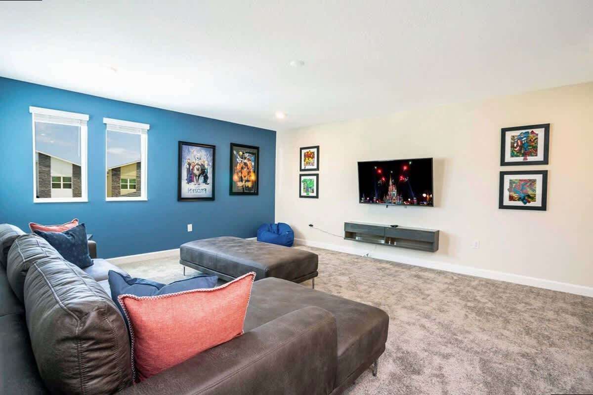 Ein Wohnzimmer mit blauer Akzentwand, einem großen Flachbildfernseher und einem grauen Sofa mit roten und blauen Kissen.