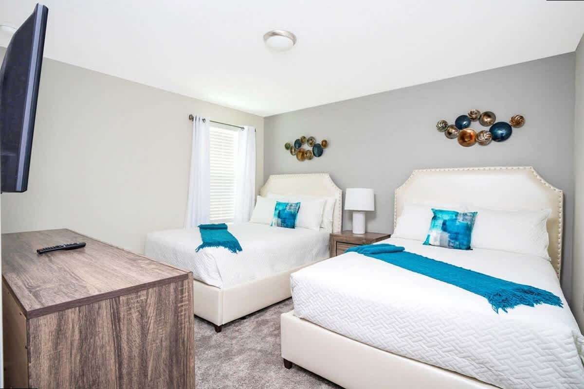 A hotel room with two beds, a TV, a wooden side table, and decorative wall art.