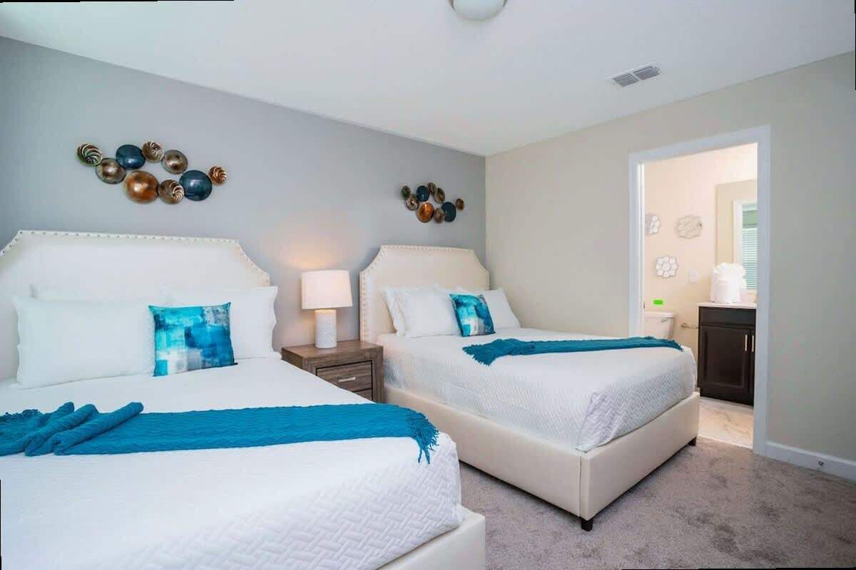 A hotel room with two beds, a nightstand, a lamp, and decorative wall art.