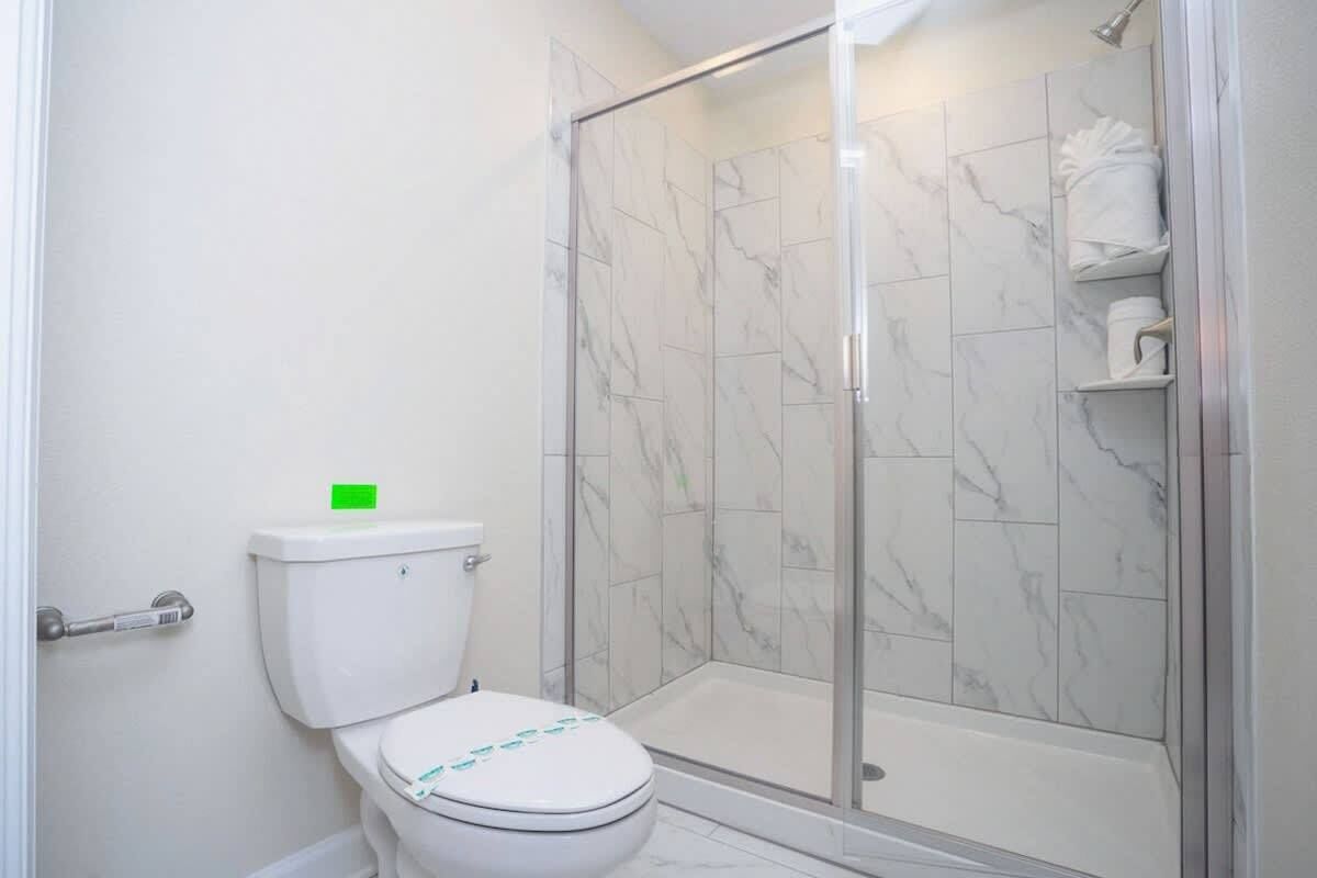 A bathroom with a toilet, a shower with glass doors, and a marble-tiled wall.