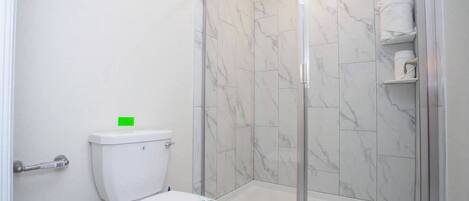 A bathroom with a toilet, a shower with glass doors, and a marble-tiled wall.
