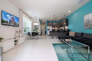 A modern living room with a black sofa, a glass coffee table, and a dining area with a white table and chairs. - Bright 5BD Disney Escape w Private Pool 1536 (Clermont)